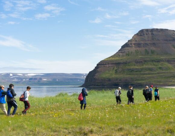 students hiking in green field with blue water behind them