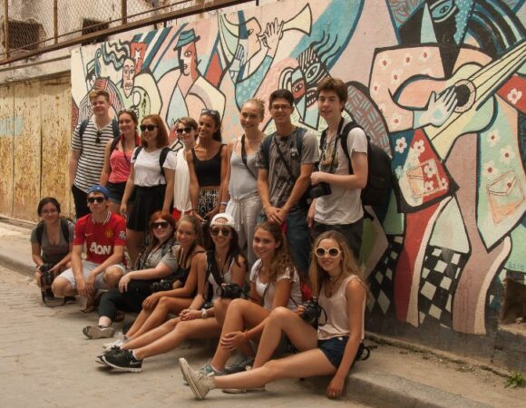 group of students smiling in front of colorful wall of graffiti