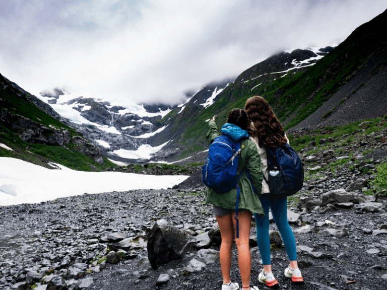 two students take a selfie in front of alaskan mountains